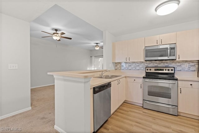 kitchen featuring decorative backsplash, appliances with stainless steel finishes, a peninsula, light countertops, and a sink