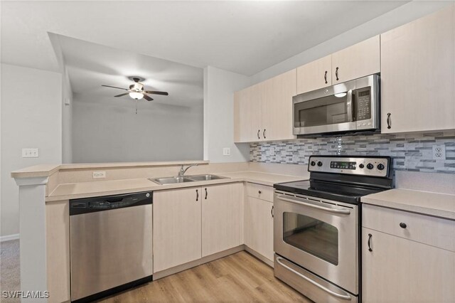 kitchen with appliances with stainless steel finishes, sink, backsplash, light hardwood / wood-style floors, and kitchen peninsula