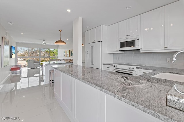 kitchen featuring sink, light stone counters, decorative light fixtures, premium appliances, and white cabinets