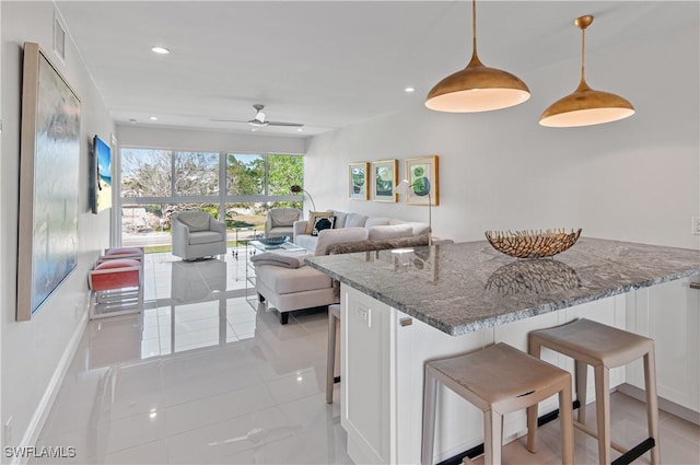 kitchen featuring a breakfast bar, pendant lighting, white cabinets, dark stone counters, and light tile patterned floors