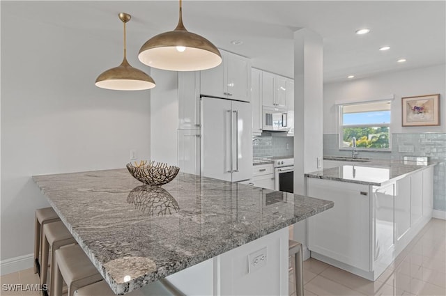 kitchen featuring pendant lighting, high quality appliances, white cabinets, a kitchen breakfast bar, and light stone countertops