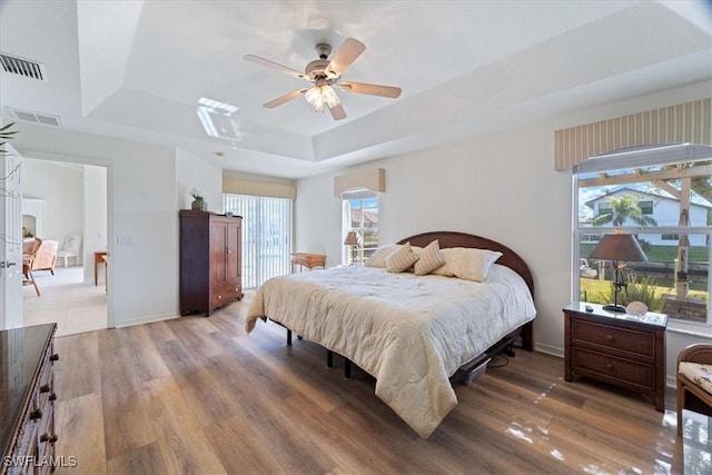 bedroom with multiple windows, a tray ceiling, ceiling fan, and hardwood / wood-style flooring