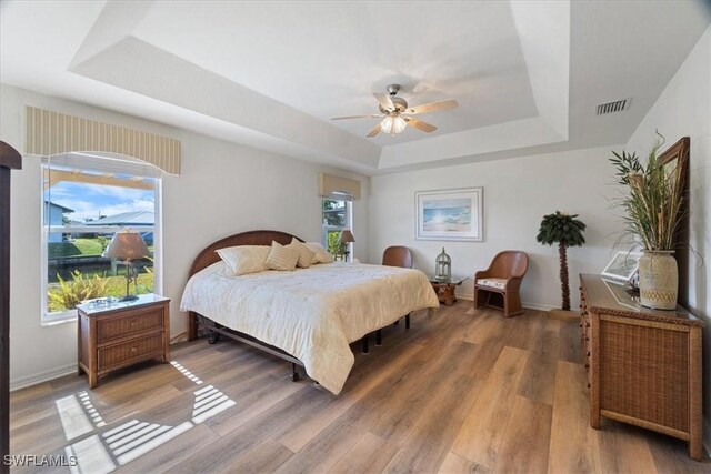 bedroom featuring ceiling fan, wood-type flooring, a tray ceiling, and multiple windows