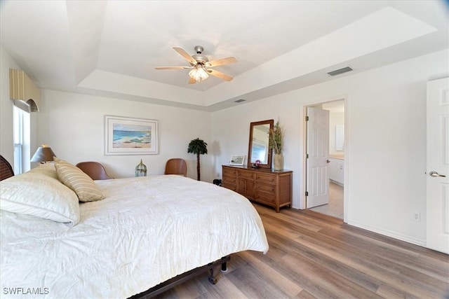 bedroom with connected bathroom, hardwood / wood-style floors, ceiling fan, and a tray ceiling