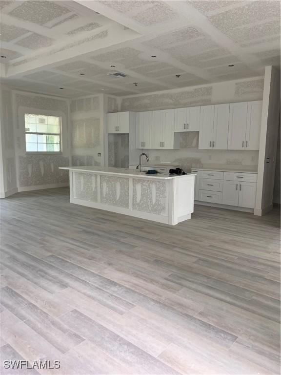 kitchen featuring light wood-style flooring, a center island with sink, and white cabinets