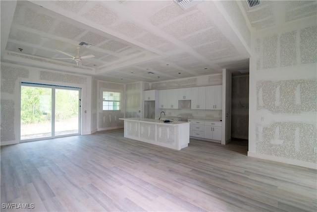 kitchen featuring a kitchen island with sink, open floor plan, white cabinets, and light wood finished floors