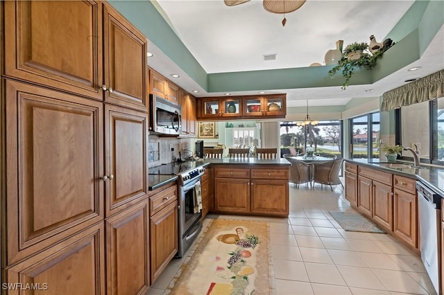 kitchen with light tile patterned floors, a tray ceiling, kitchen peninsula, pendant lighting, and stainless steel appliances