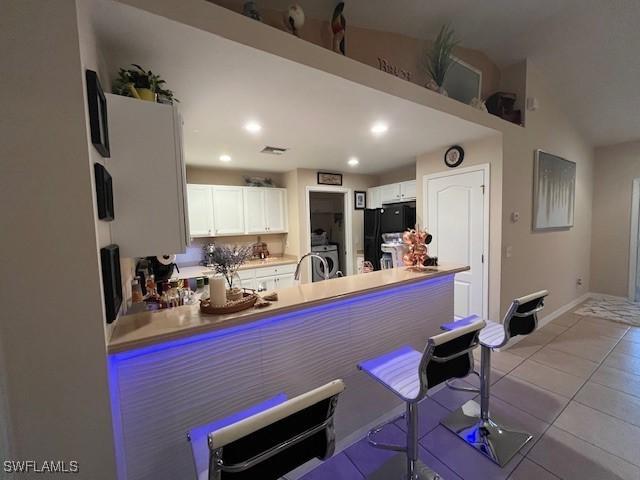 kitchen with tile patterned flooring, baseboards, a peninsula, freestanding refrigerator, and white cabinets