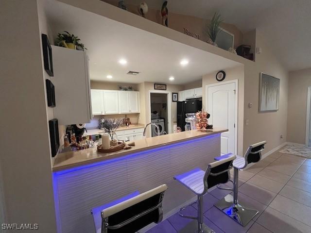 822 Johns Ave, Lehigh Acres, FL 33972 - kitchen with freestanding refrigerator, a peninsula, tile patterned flooring, white cabinetry, and a kitchen breakfast bar