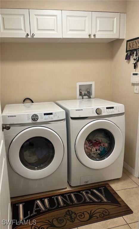 laundry area featuring light tile patterned flooring, cabinet space, and washer and clothes dryer