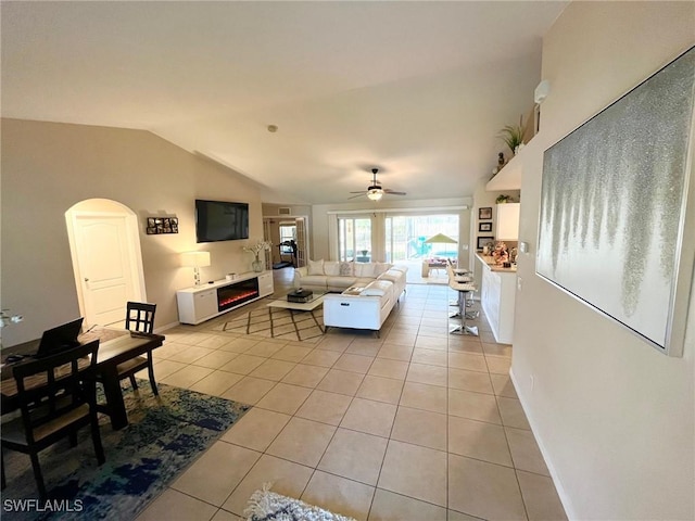 living area with light tile patterned floors, lofted ceiling, a glass covered fireplace, and a ceiling fan