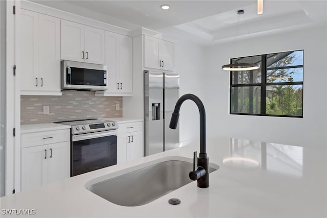 kitchen with appliances with stainless steel finishes, hanging light fixtures, white cabinets, backsplash, and a tray ceiling