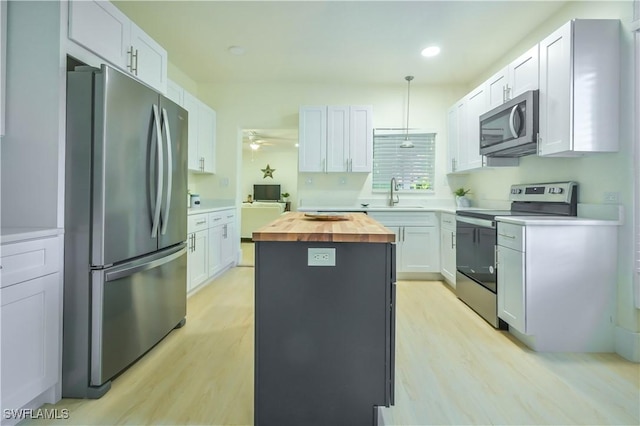 kitchen featuring butcher block counters, sink, white cabinetry, pendant lighting, and stainless steel appliances