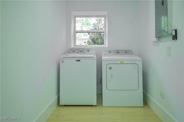 clothes washing area with electric panel, washer and clothes dryer, and light hardwood / wood-style flooring