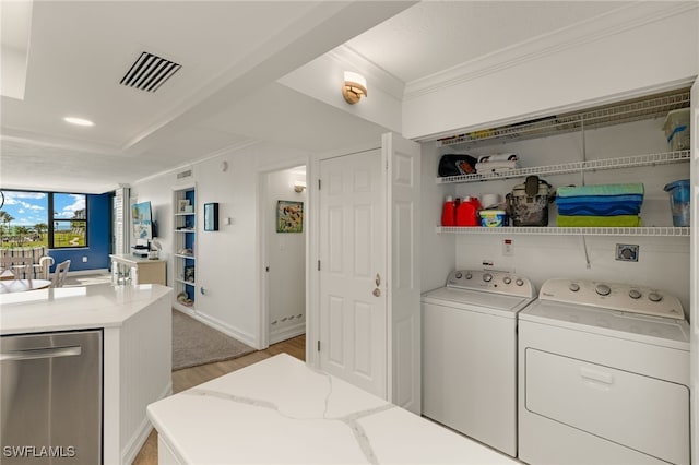 clothes washing area with crown molding, sink, light hardwood / wood-style floors, and washing machine and dryer