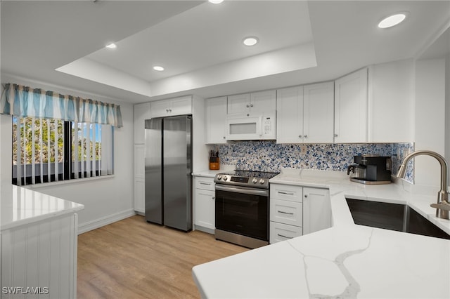 kitchen with stainless steel appliances, white cabinetry, sink, and a tray ceiling