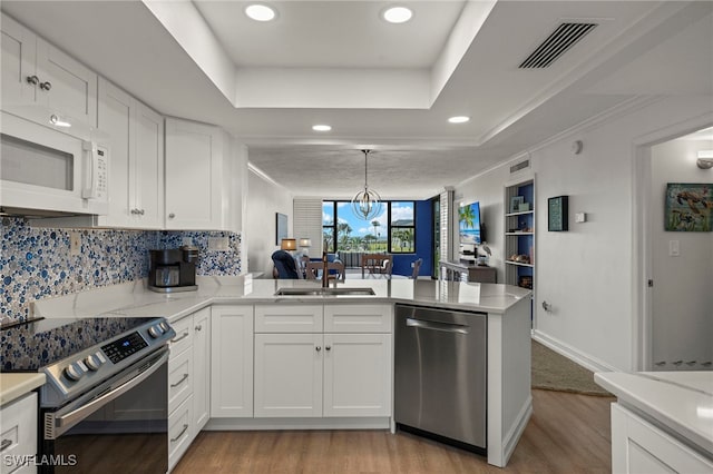 kitchen featuring sink, appliances with stainless steel finishes, kitchen peninsula, white cabinets, and a raised ceiling