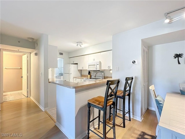 kitchen with white appliances, light hardwood / wood-style flooring, white cabinetry, a kitchen breakfast bar, and kitchen peninsula