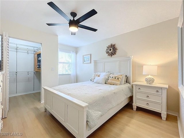 bedroom with ceiling fan, a spacious closet, a closet, and light hardwood / wood-style flooring