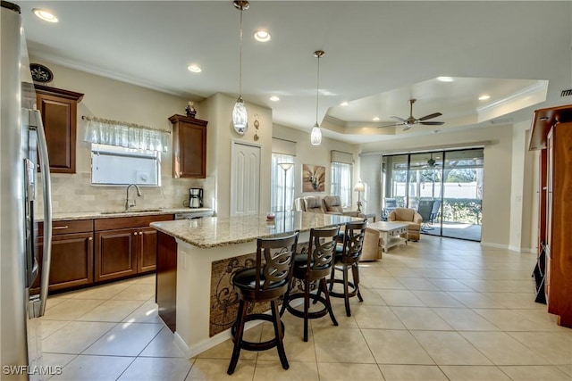 kitchen featuring sink, a kitchen island, a kitchen bar, decorative light fixtures, and a raised ceiling