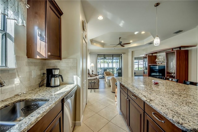 kitchen with sink, light stone counters, a tray ceiling, dishwasher, and pendant lighting