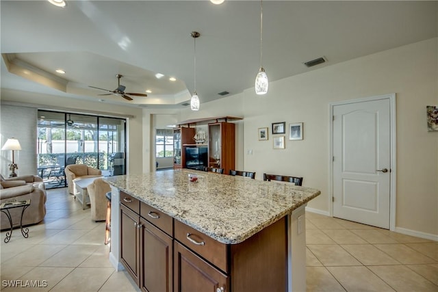 kitchen with light tile patterned floors, hanging light fixtures, a center island, light stone countertops, and a raised ceiling