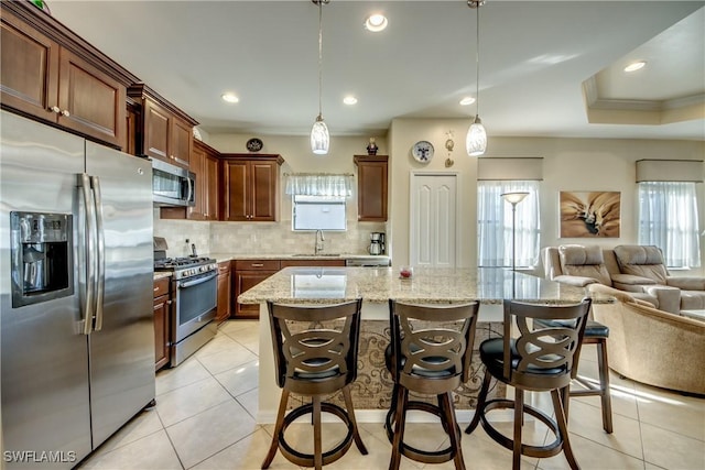 kitchen with a breakfast bar area, appliances with stainless steel finishes, hanging light fixtures, a wealth of natural light, and a kitchen island