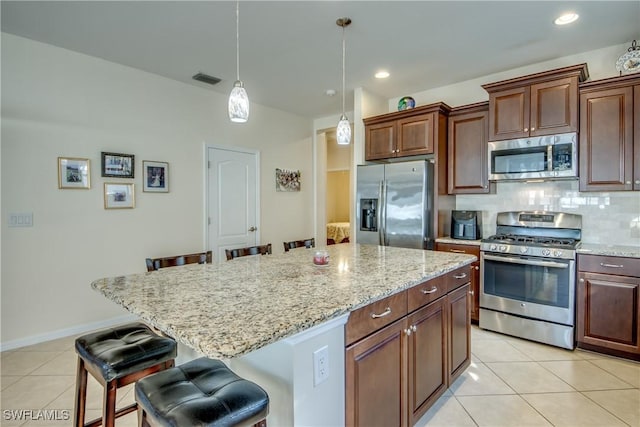 kitchen featuring a kitchen island, a breakfast bar area, decorative backsplash, hanging light fixtures, and stainless steel appliances