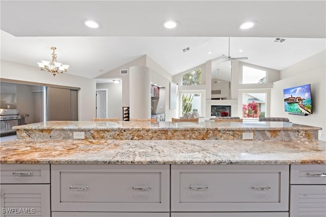 kitchen with ceiling fan with notable chandelier, gray cabinets, vaulted ceiling, and light stone countertops