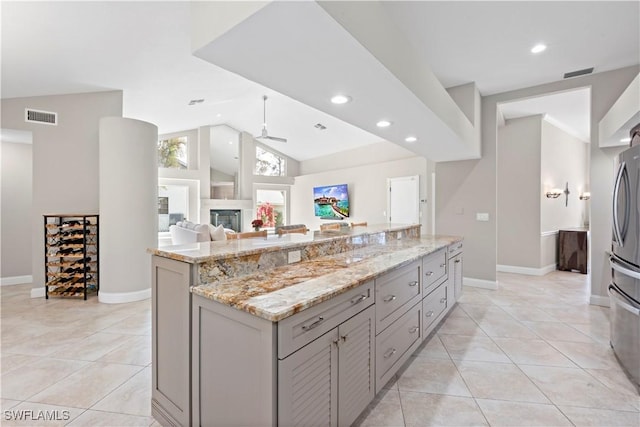 kitchen featuring a kitchen island, gray cabinetry, light tile patterned floors, ceiling fan, and light stone counters