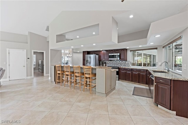 kitchen featuring sink, stainless steel appliances, a center island, high vaulted ceiling, and a kitchen bar