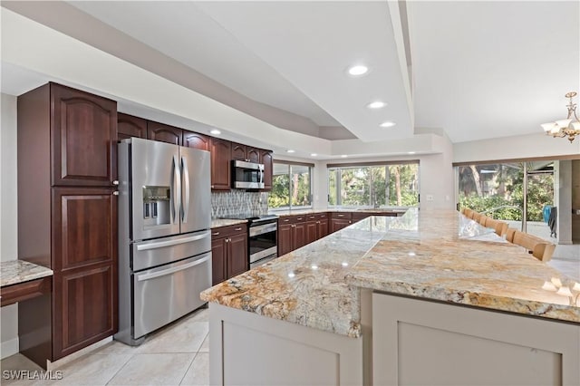 kitchen with stainless steel appliances, a notable chandelier, backsplash, and light stone counters