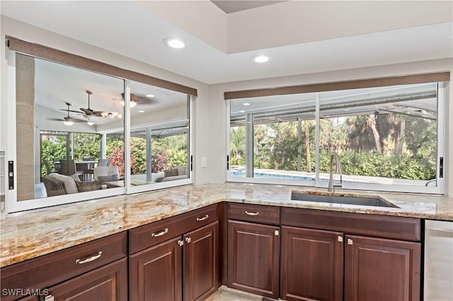 kitchen with sink, dark brown cabinets, dishwasher, ceiling fan, and light stone countertops