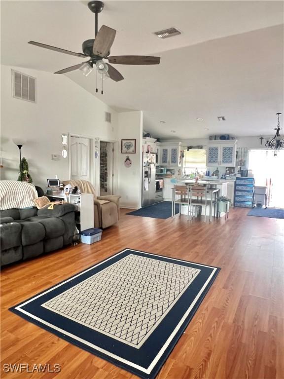 living room with vaulted ceiling, ceiling fan with notable chandelier, and hardwood / wood-style floors