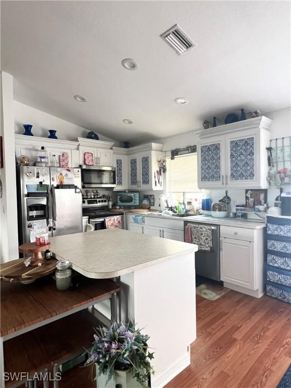 kitchen featuring vaulted ceiling, appliances with stainless steel finishes, white cabinetry, a kitchen bar, and light hardwood / wood-style floors