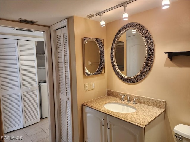 bathroom featuring tile patterned flooring, vanity, track lighting, washer / dryer, and toilet