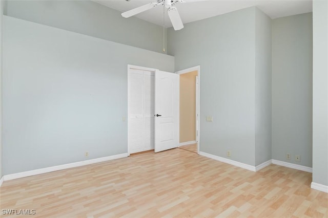 unfurnished room featuring light wood-type flooring, a towering ceiling, a ceiling fan, and baseboards