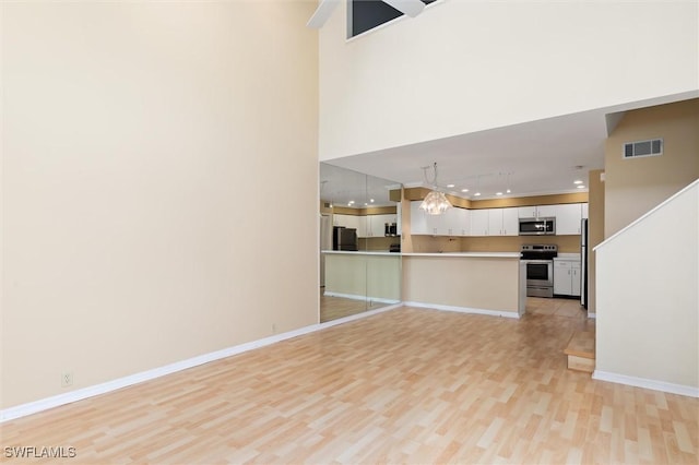 unfurnished living room featuring light wood finished floors, visible vents, baseboards, and a notable chandelier