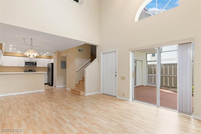 unfurnished living room featuring visible vents, light wood-style flooring, baseboards, and stairs