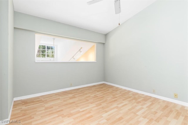 spare room with lofted ceiling, light wood-style flooring, and baseboards