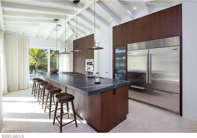 kitchen featuring a breakfast bar, lofted ceiling with beams, hanging light fixtures, stainless steel appliances, and a center island with sink