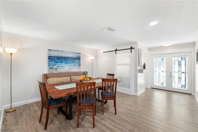 dining area with visible vents, baseboards, a barn door, light wood-style flooring, and french doors