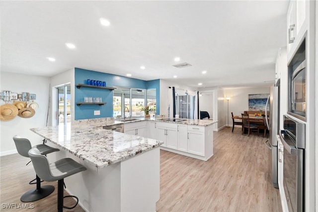 kitchen featuring a peninsula, light wood finished floors, a sink, and white cabinetry