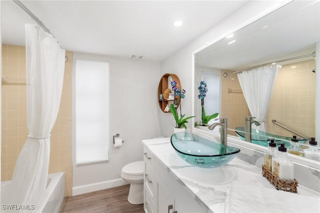 bathroom with baseboards, toilet, shower / bath combo, wood finished floors, and vanity