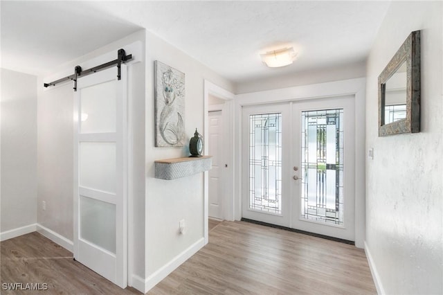 foyer featuring light wood-type flooring, french doors, a barn door, and baseboards