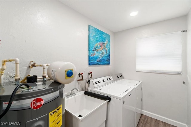 laundry area featuring wood finished floors, baseboards, separate washer and dryer, a sink, and electric water heater