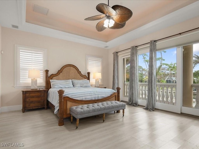 bedroom with ceiling fan, access to outside, light wood-type flooring, and a tray ceiling