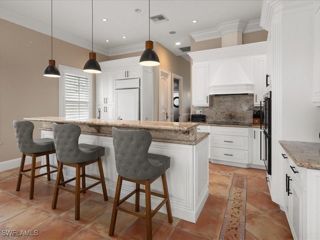 kitchen with premium range hood, decorative light fixtures, white cabinets, a center island, and light stone counters