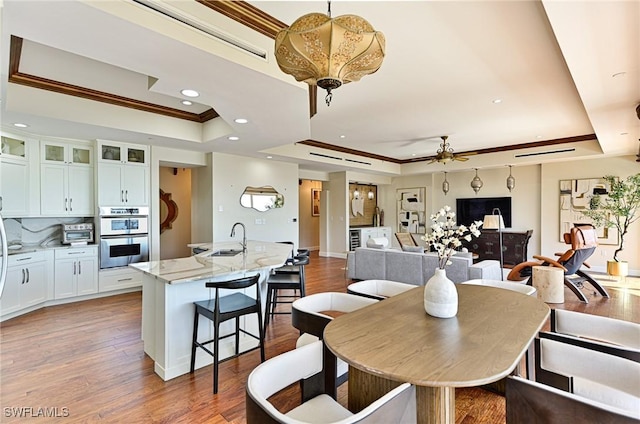 dining space featuring sink, crown molding, ceiling fan, hardwood / wood-style floors, and a tray ceiling