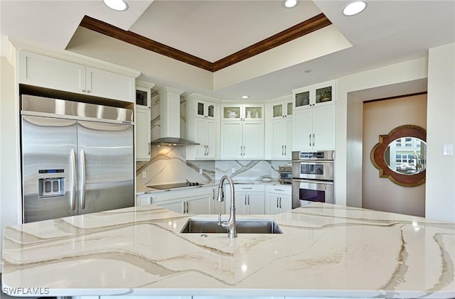 kitchen featuring appliances with stainless steel finishes, sink, wall chimney range hood, and light stone counters